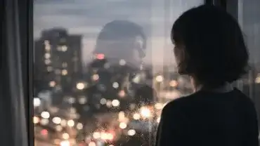 Kobieta spogląda przez okno w nocy