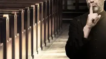 Ksiądz trzyma palec na ustach w znaku ciszy