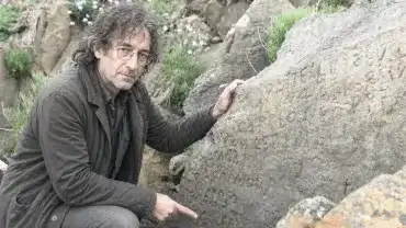 Badacz wskazujący wyryty, tajemniczy napis na skale w Plougastel-Daoulas w Bretanii